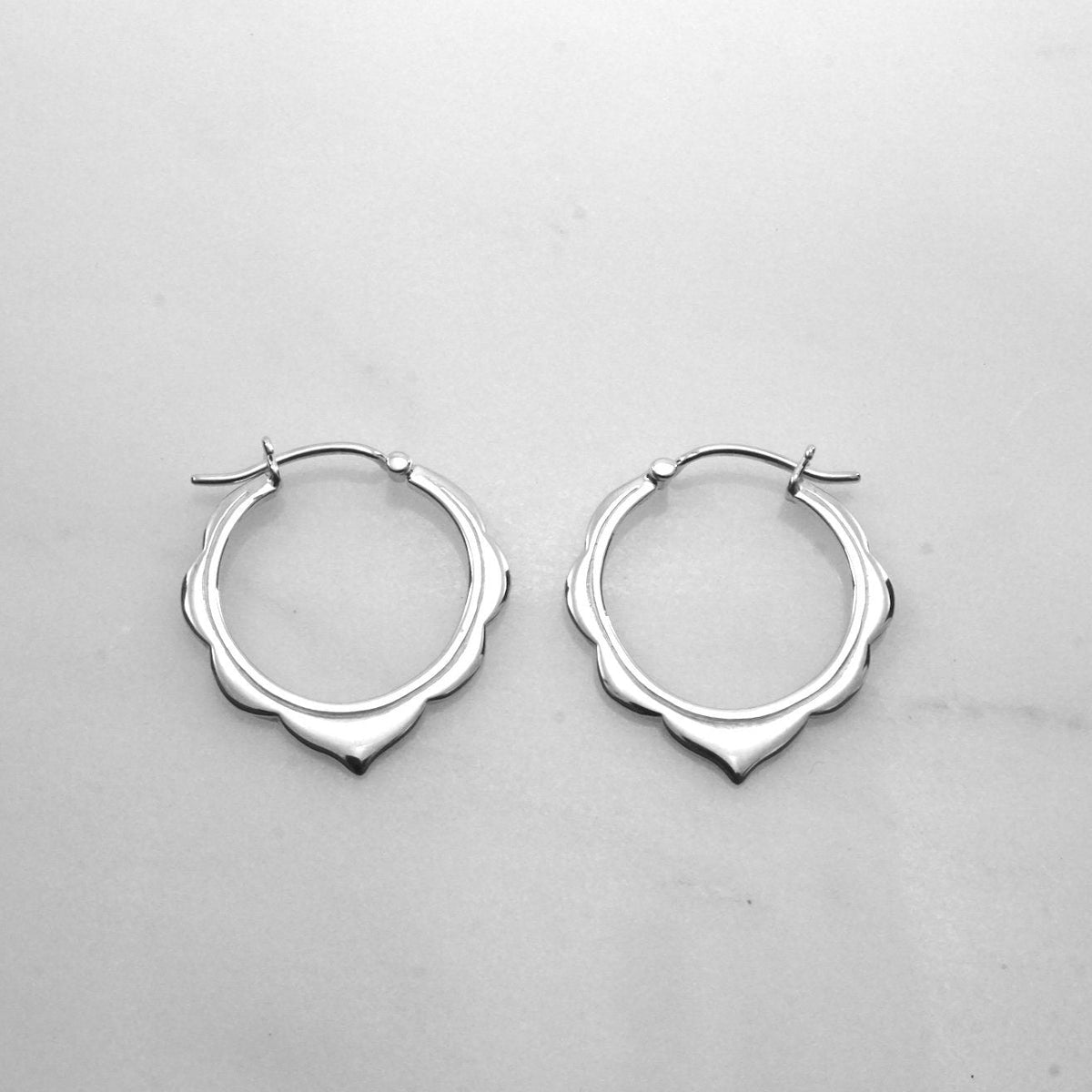 May include: A pair of silver hoop earrings with a scalloped edge.